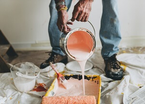 man pouring pink paint from a paint can into a roller tray