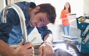 Plumber fixing tap and woman looking