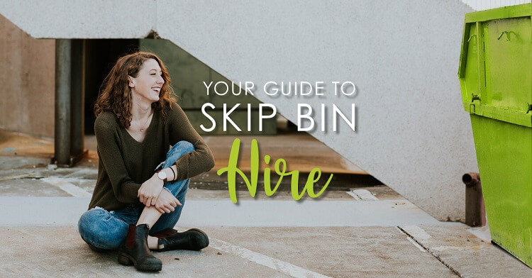 Young woman sitting on the ground laughing next to a green skip