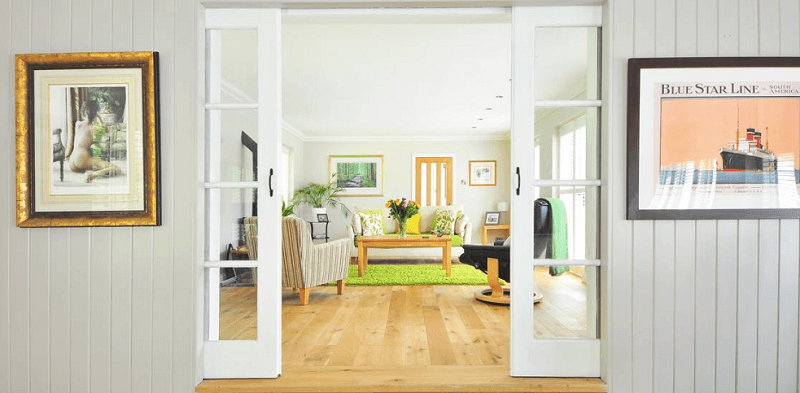 White internal doors leading into lounge with wooden floors and furniture