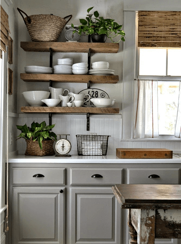 Plates stacked on wooden open shelving in traditional grey kitchen.