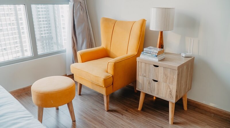 Orange arm chair and orange foot stool with small set of draws with lamp.