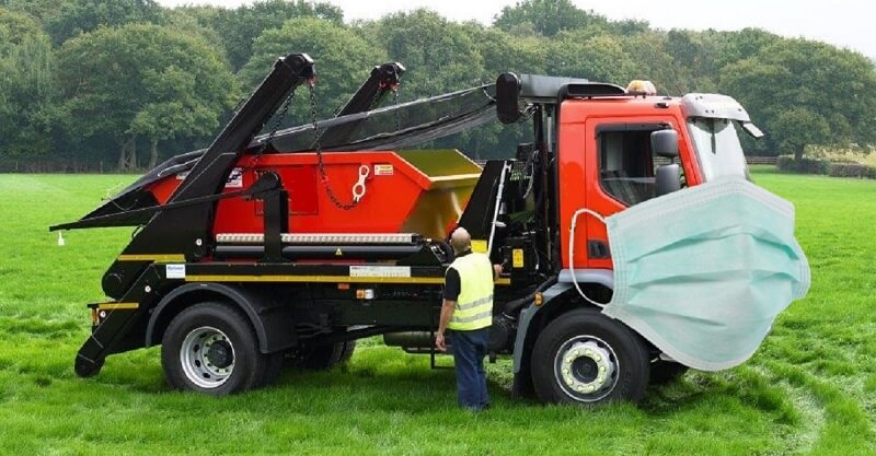 Black and red truck with a skip bin on the back. Truck is in a field with a face mask.