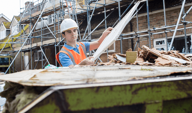 Man on building site loading rubbish in a green skip bin.