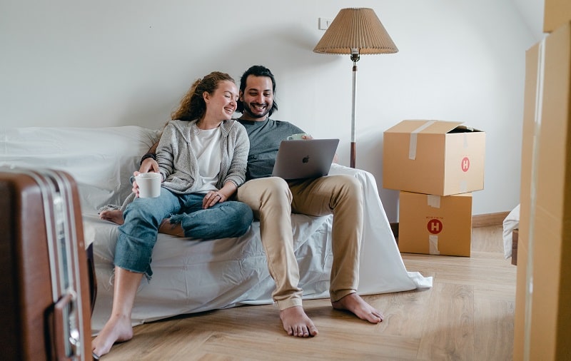 A woman and a man sitting on an old sofa while they look at a laptop computer