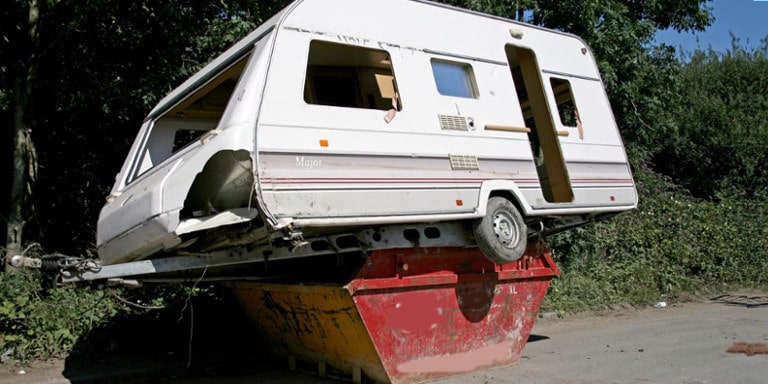 Wrecked caravan placed on top of a red skip bin