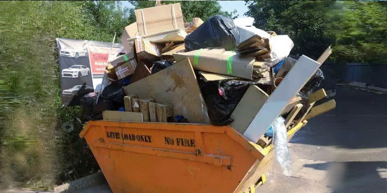 An orange skip bin that has been overfilled with cardboard, plastic and household rubbish