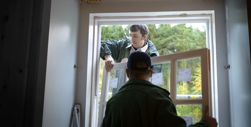 Two builders add a new window into a house.