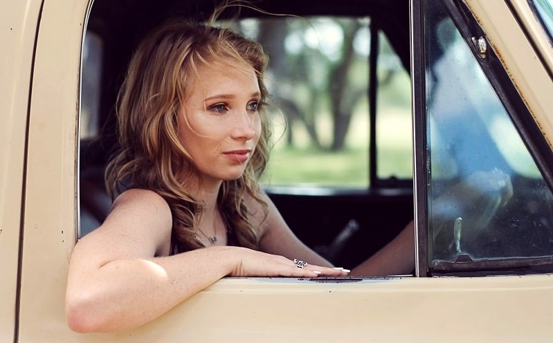 Woman in her twenties sitting inside a pickup truck with her arm outside the truck door window.