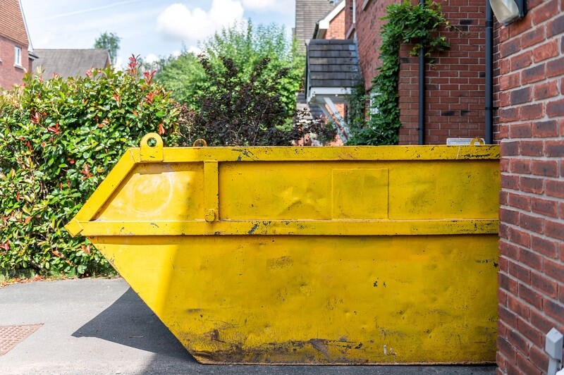 Medium size yellow skip bin outside brick house on driveway
