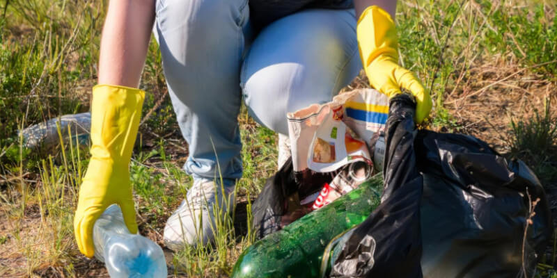 woman crouched in grass, picking up rubbish and putting it into a black plastic bag