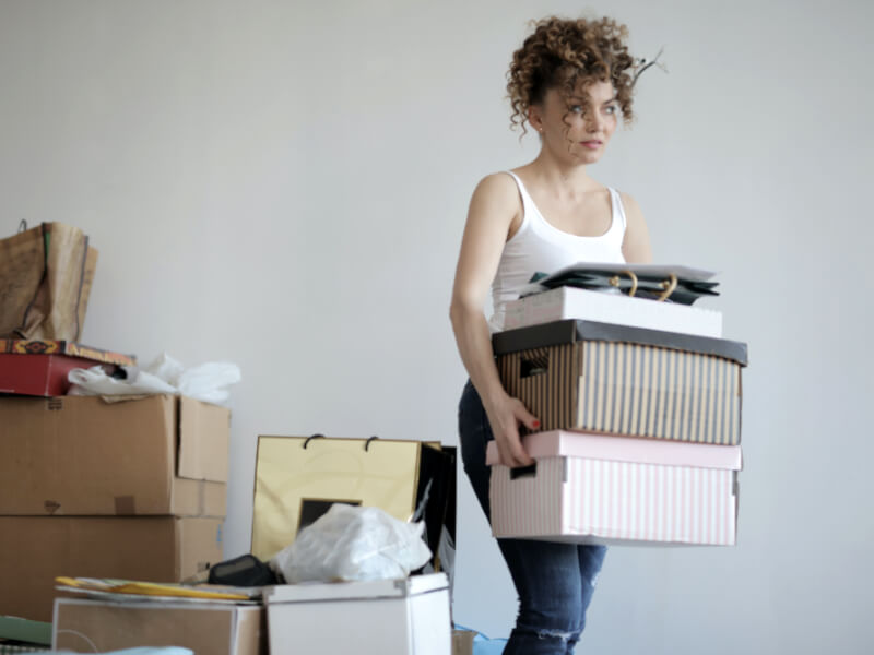 Young woman moving cardboard boxes from a cluttered stack of boxes.