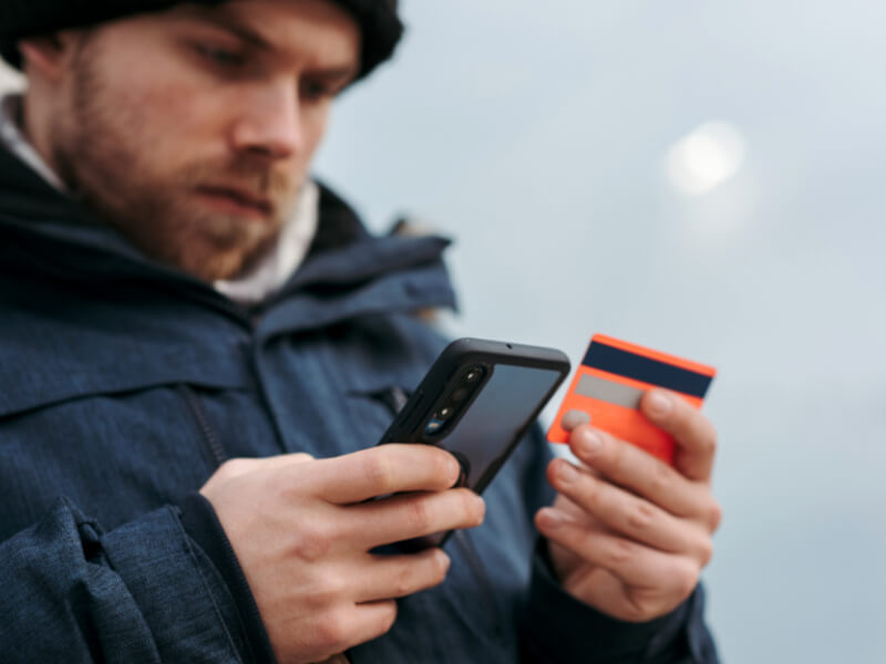 Man in his twenties looking at his mobile phone and credit card.