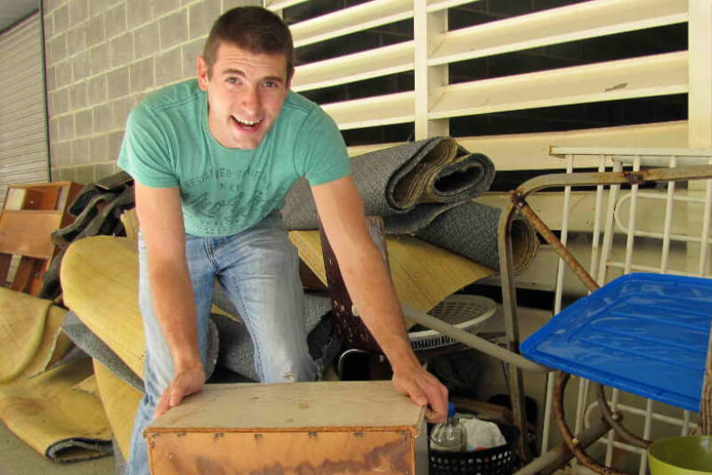 man wearing green t.shirt leaning on box and surrounded by property waste.