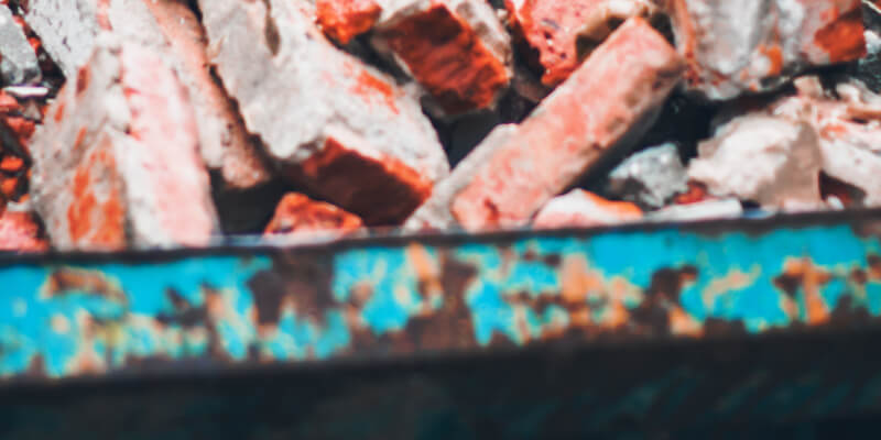 old demolition bricks loaded 
into a old blue skip bin